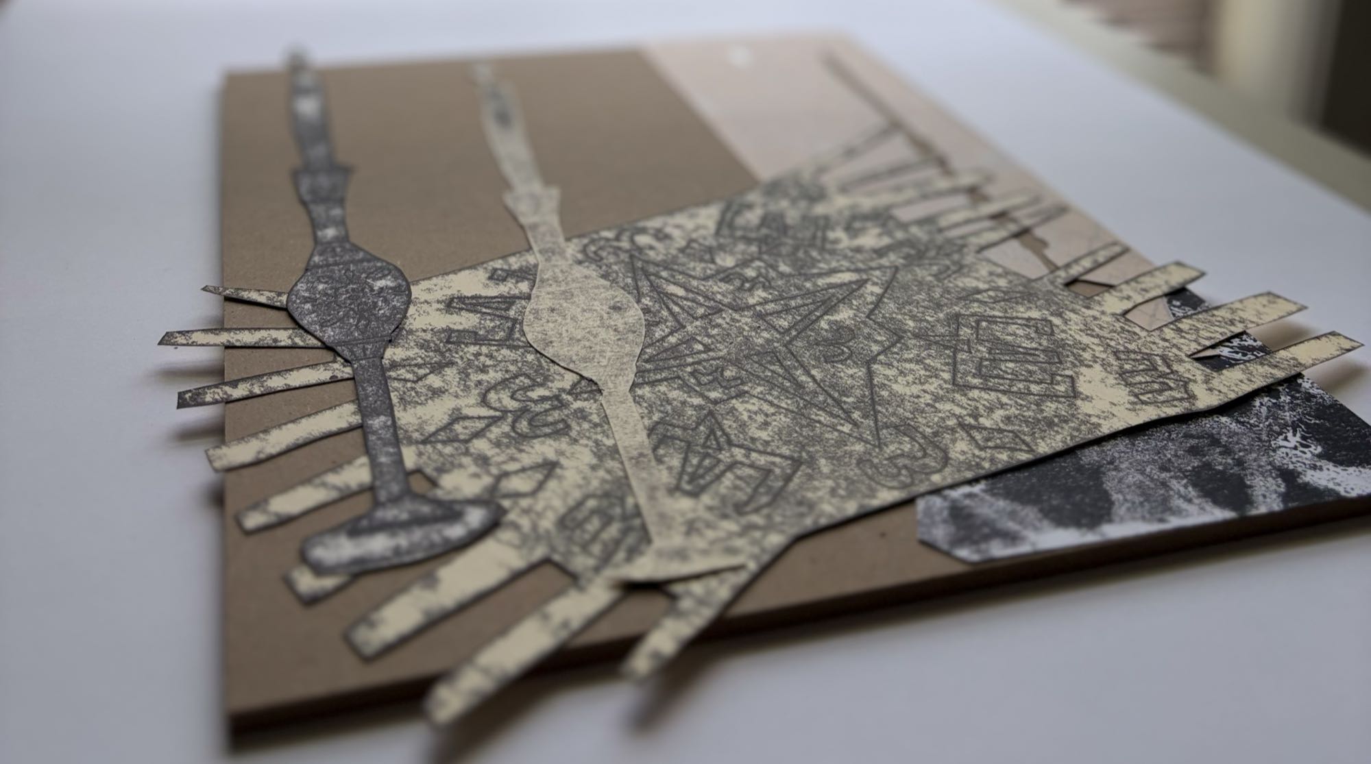 Work in progress — cut paper shapes and printed forms on cardboard